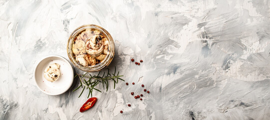 Cheese pieces with herbs and spices in olive oil in a glass jar on a light background, banner,...