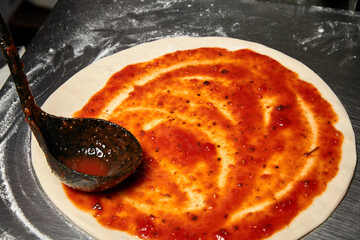 Adding tomato sauce while preparation of Italian pizza