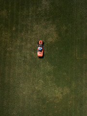 Aerial top down view of man mowing grass on football stadium. Red mower machine and driver. Minimalism. Art drone photography.