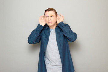 Portrait of curious man placing hands near his ears and eavesdropping