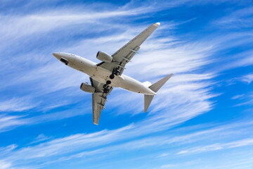 Commercial airplane flying above blue sky and white clouds.