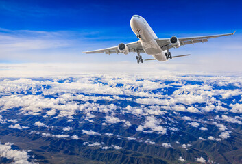 Commercial airplane flying above blue sky and white clouds.