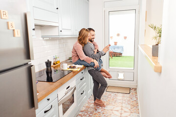 Happy young couple in kitchen at home, using mobile phone