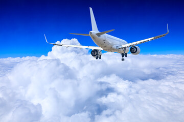 Commercial airplane flying above blue sky and white clouds.