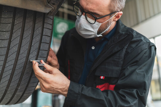 A mechanic checking the tires condition on the car lift hoist with a measuring instrument in auto service centre