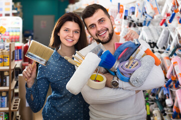 Young cheerful couple demonstrating tools for house renovating in paint supplies store