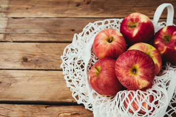 Varias manzanas dentro de una bolsa de rejilla con un fondo de madera