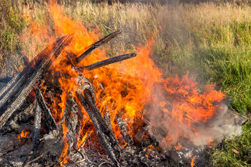 Strong bright flame of a large fire in the middle of a green field, contrasting background
