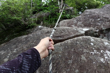 ロープを掴んで岩場を登ろうとしている男性の手