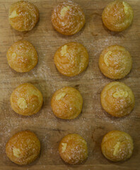 Top view of mini cream puff or profiterole with dusting powdered sugar on a wooden background. It is a pastry ball fill with whipped cream and custard. Selected focus on foregrounds.
