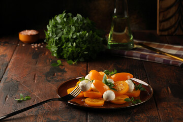 Yellow tomato salad with green basil, mozzarella balls and olive oil, seasoned with black pepper and salt. Delicious and easy snack. Vegetarian food.