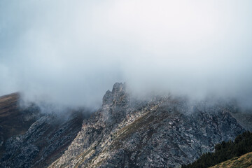Rocky mountain peak with dense fog and clouds. Winter landscape of a mysterious environment.