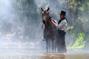 Naklejka na ściany i meble A young cowboy and a horse are relaxing by a river covered in white mist.