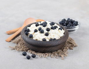 Fresh cottage cheese with blueberries in a wooden bowl on a linen napkin on a light background
