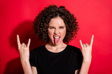 Photo of beautiful young girl tongue out hands show rock gesture isolated on vivid red color...