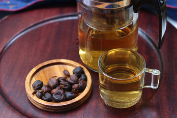 Cascara or coffee cherry tea in glass with blurred dried cherry coffee and blurred tea pot on wooden plate background. Concept for health and eco-friendly unique beverage