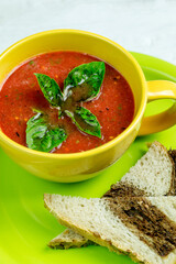 A cup of tomato soup with basil leaves and slices of bread on a green plate