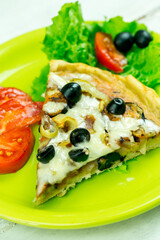 Slice of pizza on a green plate with vegetables