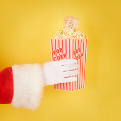 Santa Claus hand holding a red and white bucket with popcorn in yellow background
