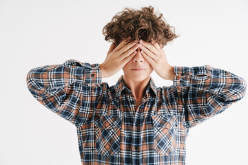 Young curly guy in plaid shirt covering his eyes