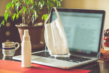 Protective mask on a laptop with a disinfectant. Coronavirus and work at home