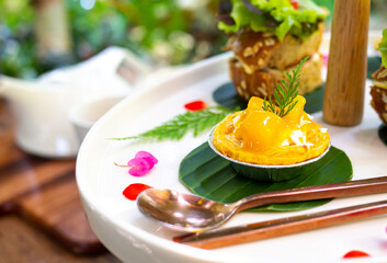 Mango tart mini is served on a white plate and adorned with beautiful flowers.