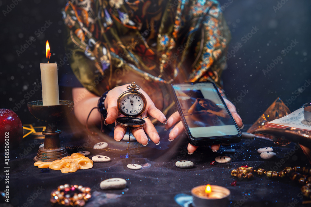 Wall mural magic and online fortune telling. the witch is holding a watch on a chain and a smartphone. close up