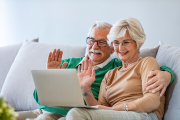 Fototapeta premium Happy senior couple having video call on laptop. Talking with grandchildren and smiling. Senior couple making video call on digital tablet with their grandchildren