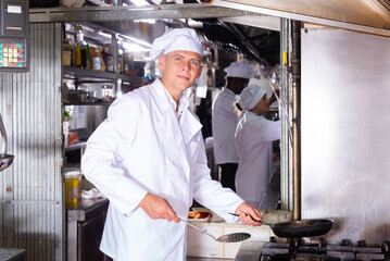 Confident experienced chef in white uniform working in professional kitchen of restaurant