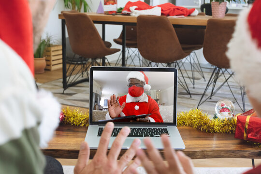Rear view of man and son in santa hats waving while having a videocall with santa claus wearing face