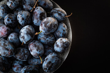 Ripe Plums in bowl. Top view against black background