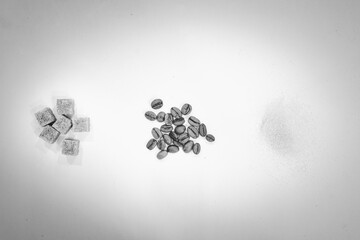 Black and white image of coffee beans surounded by granules of white sugar and cubes of brown sugar.