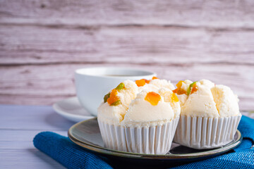 Side view of Thai steamed cupcakes topped with dry fruit on a plate on blue cloth and a cup of white coffee with a wooden background. (Khanom Pui Fai in Thai)