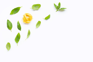 Raw tagliatelle pasta with basil leaves on white background.