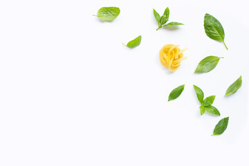 Raw tagliatelle pasta with basil leaves on white background.