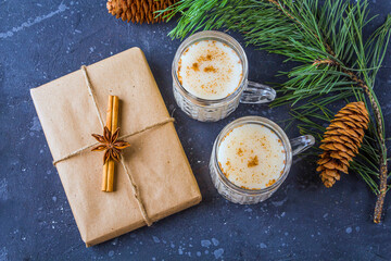 Traditional American and Kandacian Christmas drink eggnog in crystal glasses with cinnamon and fir branch, cone. New Year Gift box decorated with cinnamon stick and anise star. Winter holidays