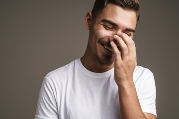 Image of joyful unshaven guy laughing and covering his face