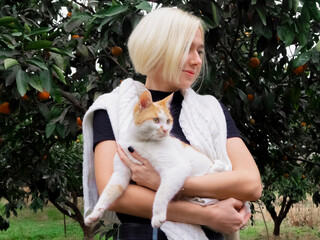Blonde girl in a tangerine garden holding a white cat in her arms