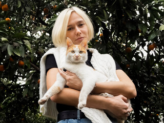 Blonde girl in a tangerine garden holding a white cat in her arms