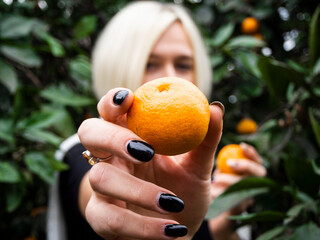 Blonde girl in a tangerine garden holding two tangerines in her hands