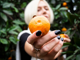 Blonde girl in a tangerine garden holding two tangerines in her hands