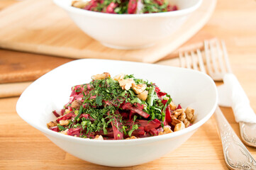 Delicious salad with boiled beets and nuts. Beautiful serving of the dish in a white bowl