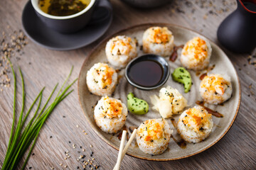 Baked sushi maki rolls with prawns and crab on a plate with chopsticks, soy sauce, wasabi and ginger. Japanese traditional fish food closeup served for lunch in modern gourmet restaurant