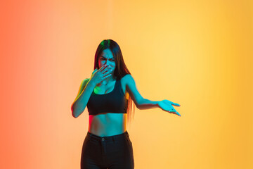 Disguasted, disappointed. Young caucasian woman's portrait on gradient yellow-orange studio background in neon light. Concept of youth, human emotions, facial expression, sales, ad. Copyspace for ad.