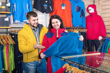 Smiling happy couple examining track jackets in sports clothes store