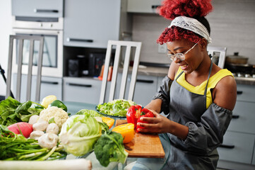 African american woman preparing healthy food at home kitchen. She cuts red pepper.