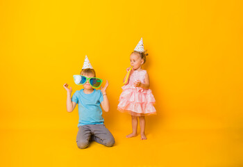 a little boy and girl in holiday caps are playing whistles on a yellow background with a copy of...