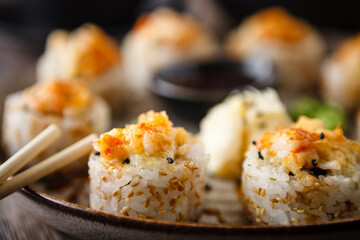 Baked sushi maki rolls with prawns and crab on a plate with chopsticks, soy sauce, wasabi and ginger. Japanese traditional fish food closeup served for lunch in modern gourmet restaurant