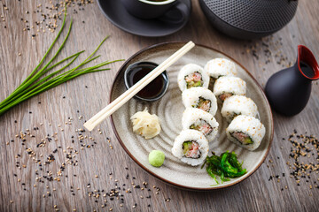 Sushi maki rolls California with crab, cucumber and avocado on a plate with chopsticks, soy sauce, wasabi and ginger. Japanese traditional seafood served for lunch in modern gourmet restaurant