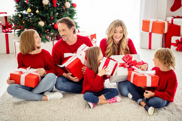 Obraz na płótnie Canvas Photo of full family five people gathering three small kids sit carpet exchange big boxes present wear red jumper jeans in living room x-mas tree garland many gifts indoors